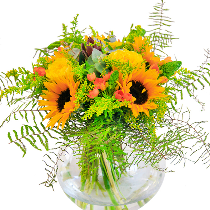 Perfect for any joyful occasion, this sumptuous bouquet-expertly arranged right in the heart of Chingford-captures the lively transition from late summer to autumn. Sunflowers shine at the center, their star-shaped faces and golden petals echoing the soft morning glow that washes over Connaught Waters. Nestled around these bold flowers, yellow garden roses bloom in tightly layered swirls, their classic appeal further enriched by the presence of glossy, bright red hypericum berries scattered throughout. Ferns and fine, trailing greens spill over the rim, evoking the abundance of nearby woodland walks and lending a gentle, natural flow to the display. Touches of feathery goldenrod, light green spikes, and soft-edged eucalyptus leaves peek out, weaving subtle hints of color and fresh scent through the bouquet. The clear, spherical vase anchors the stylish composition, promoting clarity and letting each vivid stem be seen in the water below. Every element is thoughtfully placed, combining rich textures-the velvety sunflowers, the crispness of foliage, the smoothness of berries-to evoke comfort and celebration. Whether placed on a dining table for a birthday dinner or delivered as a cheerful 'thinking of you' gift to a home along Kings Head Hill, this arrangement radiates the authentic spirit and fresh beauty of Chingford.