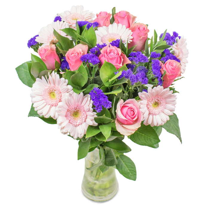 This standout bouquet, prepared by Chingford Florist, features a radiant mix of flowers presented in a crisply transparent glass vase set against a clean white background. The centerpiece includes approximately 7-9 soft pink roses, their petals at various stages of opening, showcasing classic spiral shapes and delicate hues, each one selected for its freshness. Balanced alongside are about 5-7 large-headed Gerbera daisies in pale, blush pink, their wide petals and creamy centers adding openness and charm. Rich, vibrant clusters of purple statice are interwoven, offering a dramatic textural and visual contrast, akin to wild blooms growing near Chingford Mount. The bouquet's deep green foliage forms a plush, abundant base, reinforcing the freshness and vitality of each stem. The vase's clear sides display sturdy stems and pristine water, indicating same-day preparation and local delivery. Perfect for marking birthdays, anniversaries, or brightening a desk in a Chingford office, this arrangement radiates joy and affection reflective of the area's welcoming community.